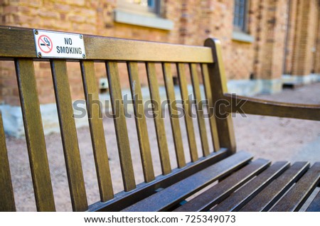 No smoking sign attached on the wooden park bench.