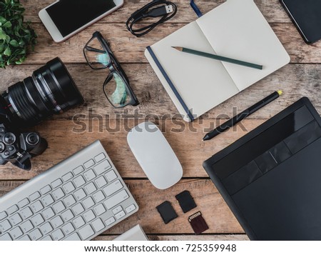 top view of photographer work station, work space concept with digital camera, notebook, memory card, smartphone, graphic tablet, external harddisk on wooden table. Royalty-Free Stock Photo #725359948
