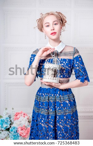 Cute young woman in navy blue dress holding bird cage, spring tender fashion studio shot