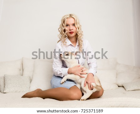 blonde woman sitting on a sofa with puppy husky dog. girl playing with a dog