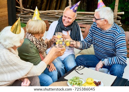 Portrait of smiling senior man wearing party hat toasting with group of friends while celebrating his birthday at outdoor cafe