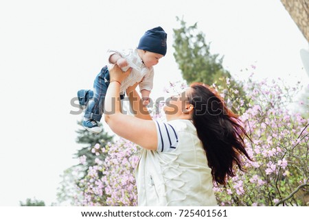 Mother throws baby up to the sky, laughing and playing in the spring on the nature blooming background