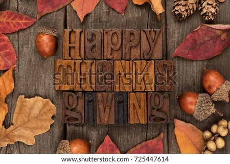 Happy Thanksgiving spelled with wooden letterpress with frame of autumn leaves over a rustic wood background