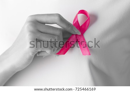 Close-up of a woman in white t-shirt holding a breast cancer awareness pink ribbon on her chest with one hand. Color pass. Black and white picture. Healthcare medical concept.