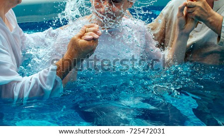 Two pastors baptize a man in the name of Christ Royalty-Free Stock Photo #725472031