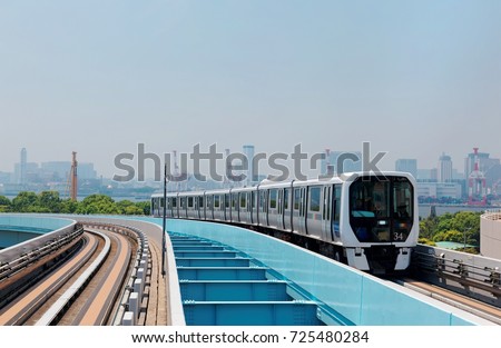 Scenery of a train traveling on the elevated rail of Yurikamome Line in Downtown Tokyo, with a background of modern buildings in Odaiba under blue clear sunny sky Royalty-Free Stock Photo #725480284