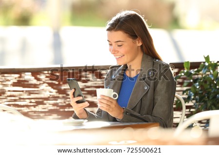 Single fashion teen using a smart phone sitting in a coffee shop terrace with a back light in the background