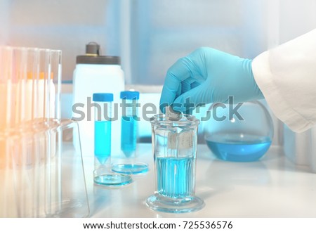 Scientific background with microscope room and microscopic slide in gloved hand. Shallow DOF,toned image, focus on the hand. Pencil writing here was generated for this photo session. 