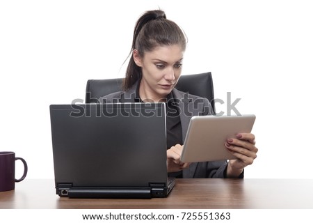 business woman sitting at her desk working on a laptop and tablet computer