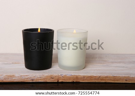 White and black candles. Two burning candles on wooden table against white wall. Royalty-Free Stock Photo #725554774