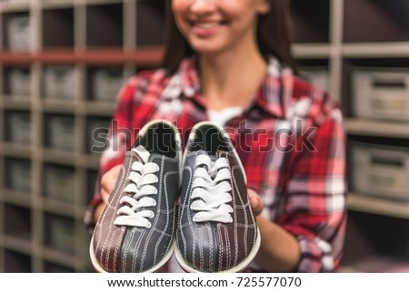 Cropped image of beautiful girl holding a pair of bowling shoes and smiling, shoes in focus