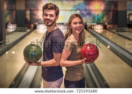 Beautiful girl and handsome guy are holding bowling balls, looking at camera and smiling ready to play