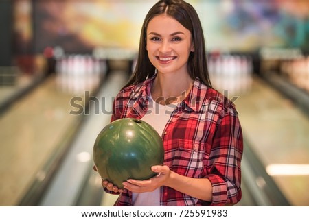 Beautiful girl is holding a bowling ball, looking at camera and smiling ready to play bowling