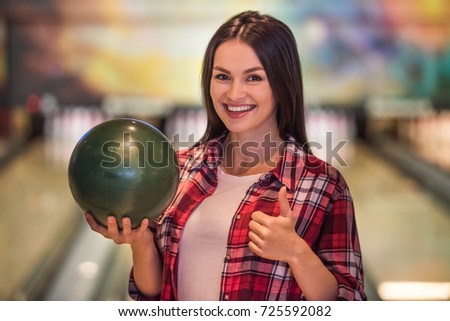Beautiful girl is holding a bowling ball, showing Ok sign, looking at camera and smiling ready to play bowling