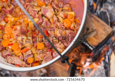 Boiling, hot goulash soup with meat, paprika, potatoes, onion, carrots is the traditional dish of Hungarian cuisine. Meat stew being prepared in crock pot on open fire. Picnic at the weekend in nature