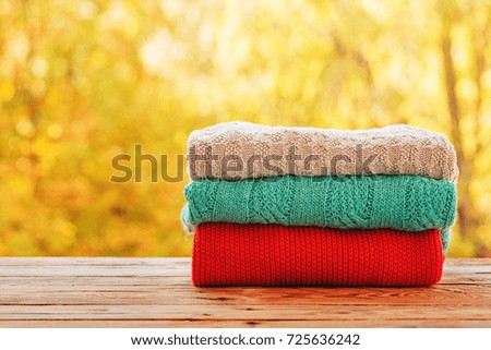 Stack pile of cozy colorful knitted sweaters on autumn nature background. Concept warm clothing.