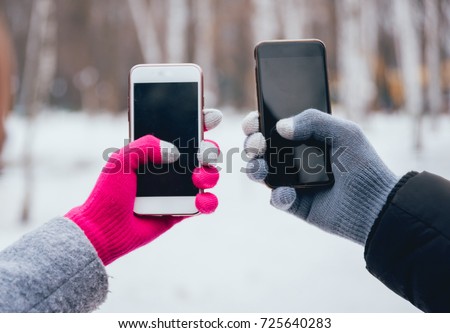 Couple using smartphone in winter with gloves for touch screens. Backgound