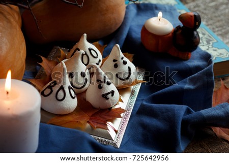 Funny meringue ghosts for Halloween party on autumn decorations. Golden leaves, pumpkin, blue textil and light of candles. Halloween concept