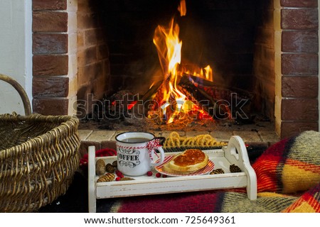 A fire in the fireplace. Warm cozy place with orange bonfire. A cup of coffee and a slice of bread with jam on a tray in front of the fireplace. Royalty-Free Stock Photo #725649361
