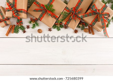 Gift boxes, nuts, small bells and fir tree twigs border, top view with copy space on wood table background. Frame of colored packages with red, green ribbons for christmas, valentine day or birthday