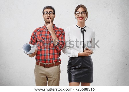 Worried clunky male architect in big spectacles with thick lenses and his pretty female wait for boss, being nervous as present their decisive project. Geek man and female companion work together