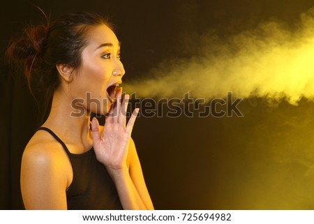 Smoking Tan Skin Asian Woman black hair dark lip with Yellow Dense Fluffy Puffs of Smoke and Fog on dark Background, Abstract Smoke Clouds, and high low exposure contrast, copy space for text logo