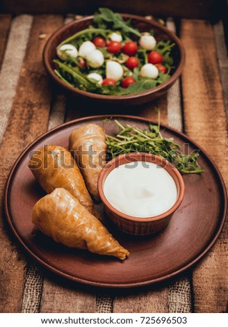 Tasty meat rolls with sour cream and salad on wooden table