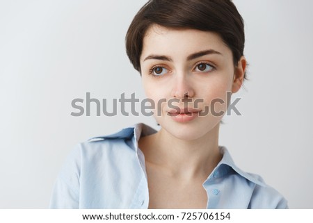 Close up portrait of beautiful caucasian girl with short dark hair and big brown eyes looking aside, smiling gently with relaxed look.