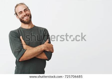 Attractive swedish man with stylish hair and beard laughs at funny story from friend with crossed hands and closed eyes.
