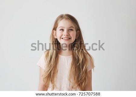 Portrait of cute little girl with long light hair smiling brightfully, looking upside on colorful flying balloons with happy and excited expression.