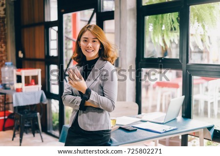Smiling Business woman working in office with documents,Happy Asian businesswoman using phone sitting on chair at modern home studio.Concept of young people working mobile devices,contact to costumer Royalty-Free Stock Photo #725802271