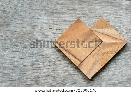 Tangram puzzle in heart shape on wood background