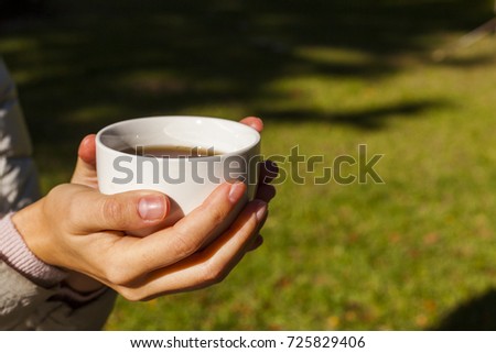 A young woman is holding a white cup with a hot tea with both hands.