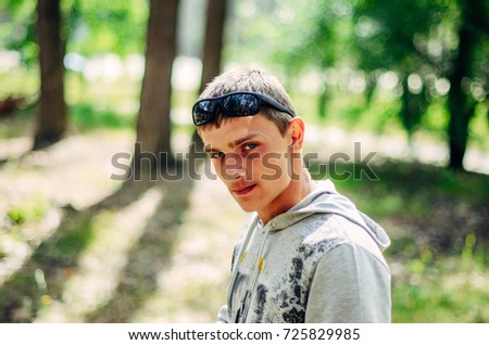 a young man walks in the woods. on it wearing sunglasses , jeans and a sweatshirt