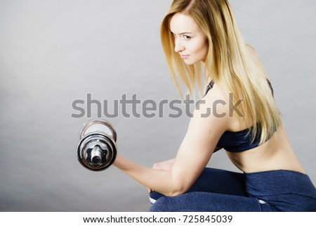 Strong woman lifting dumbbells weights. Fit girl attractive blonde model exercising gaining building muscles. Fitness and bodybuilding, on grey