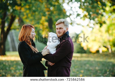 young family and newborn son posing for the camera in autumn park