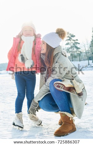 Mother helps daughter with ice skating in winter