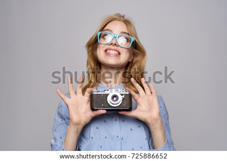woman photographer with a smile in glasses holds an old-fashioned camera on a gray background                               