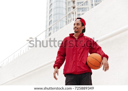 Picture of handsome young african man walking outdoors. Looking aside play basketball.