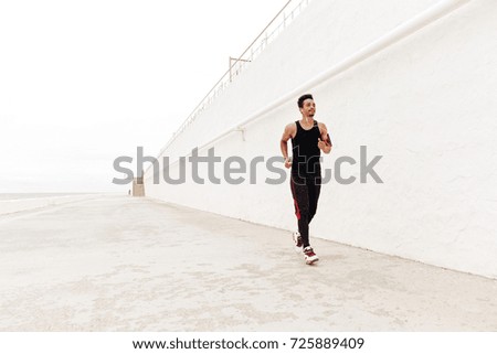 Picture of concentrated young african sports man running outdoors. Looking aside listening music.