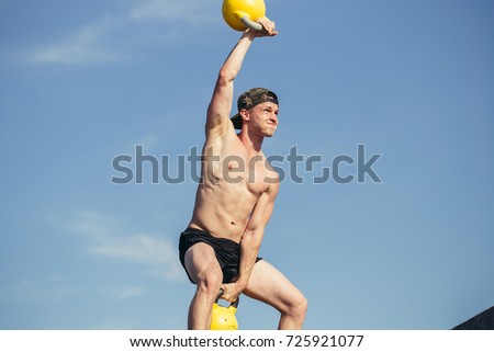 Low section portrait of unrecognizable man lifting two heavy kettlebells with vigorous effort during workout on gym