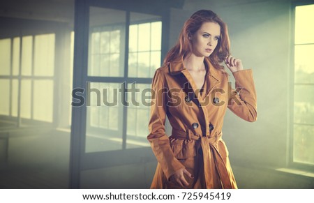 Beautiful fashionable girl stands near the window wall . Smoke cinema photo