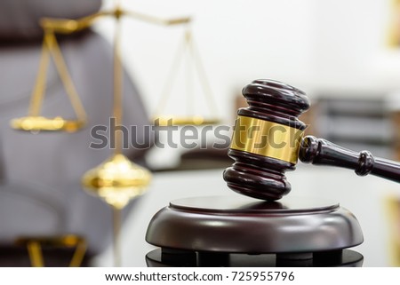 Legal office of lawyers, justice and law concept : Wooden judge gavel or a wood hammer and a soundboard used by a judge person on a desk in a courtroom with a blurred brass scale of justice behind. Royalty-Free Stock Photo #725955796