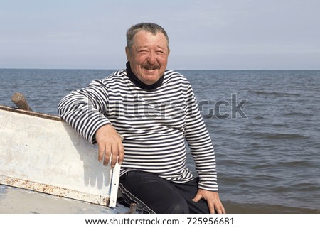 Â  Portrait of a mature man on a light dyural boat on the shore of Lake Baikal.
The skipper sits on the bow of the boat on the shore of Lake Baikal.