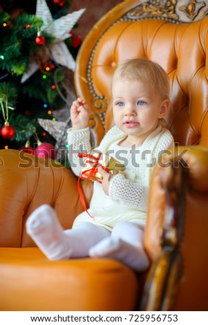 happy little girl with a gift in her hands sits on a chair, in the background a festive Christmas tree