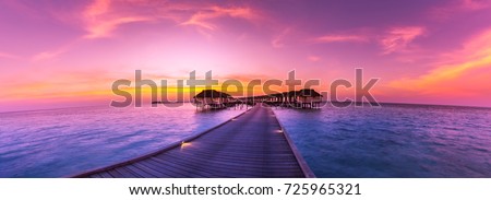 Amazing sunset panorama at Maldives. Luxury resort villas seascape with soft led lights under colorful sky. Royalty-Free Stock Photo #725965321