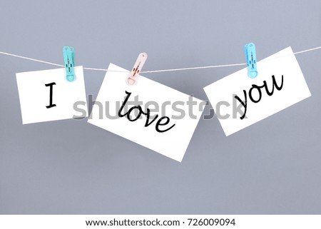 Words I love you on the white paper and hanging on the cord. Over gray background.