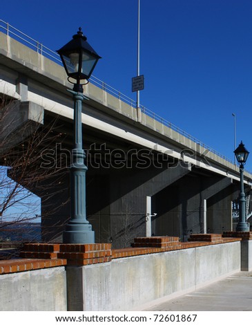 A Bridge running parallel along a parking lot wall and lamp posts with a bright blue sky and room for your text.