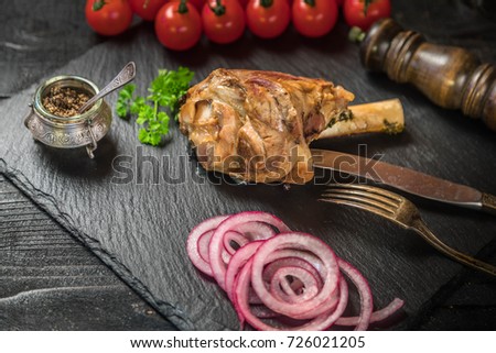 Lamb shank dinner on slate tray with vegetables, parsley and mint jam on black rustic wooden table, top view, copy space