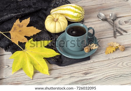 A cup of tea, autumn leaves, pumpkins and black lace on a wooden table close-up. Design of the table for the autumn holidays. 